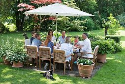 Gäste an gedecktem Tisch unter Sonnenschirm im Garten