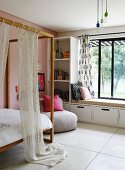 Canopied bed with wooden frame next to shelves and window seat in modern, child's bedroom