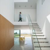 Staircase with glass balustrade in minimalist interior with dining table in front of sliding terrace doors in background