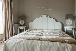 Double bed with white, ornate wooden headboard against taupe wall in elegant bedroom