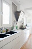 Long white kitchen counter with twin sinks and metallic wall tiles