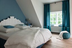 Bedroom with blue accents: double bed with white, carved headboard against blue-painted wall and blue, floor-length curtains