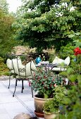 Gartenplatz mit schwarzen Metallstühlen und hellen Sitzpolstern um runden Tisch