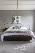 Felldecke auf Bett vor grauer Stuccolustrowand mit weißem Deko-Buchstabe