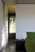 Bett vor weißer Wandscheibe mit Schwenktür in minimalistischem Schlafzimmer
