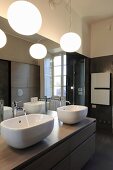 Twin sinks on washstand below large mirror and spherical lamps in bathroom