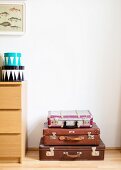 Stack of vintage suitcases next to chest of drawers with round boxes on top
