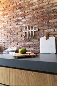 Magnetic knife rack on brick wall above grey kitchen worksurface