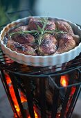 Grilled chicken legs and sprigs of rosemary in white flan dish on top of fire basket with barbecue grille
