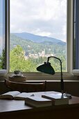 Blick über Schreibtisch mit nostalgischer Tischleuchte und Büchern auf Hügellandschaft