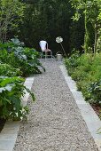 Gravel path with stone edging leading to vintage garden chair and watering can in front of green hedge