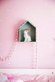Rabbit figure on house-shaped shelf with pearl necklace on pink wall