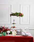 A table decorated for Christmas with a red tablecloth and white crockery, a Christmas wreath hanging above