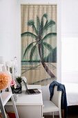 White desk and chair in front of bamboo wall hanging with palm tree motif