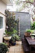 Gartentisch und Bank auf begrünter Terrasse mit Pflanztöpfen vor grauer Sichtschutzwand