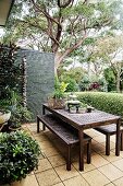 Table and bench set on a green terrace in front of box hedge and screen wall
