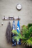 Wall hook strip with towels and a dried branch next to a palm tree against a gray wall