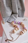 A homemade necklace of wooden beads strung on a leather cord on a white chair with a ring