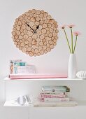 DIY wall clock made from round pieces of rustic birch wood above a stack of books and a vase of flowers on a white shelf