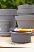 Grey painted flowerpots with a brush on a terracotta bowl in the foreground