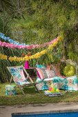 Deckchair and cushions below garlands in colourful seating area in garden