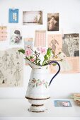 Rosen in einer alten Emaillekanne vor Wand mit nostalgischen Bildern