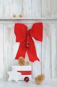 Wrapped gift and golden pine cones below large red bow on white board wall