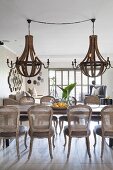 Vintage cane-back chairs around dining table below two large wood-and-metal chandeliers