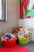 Bunte Plastikwannen mit Plüschtieren in Kinderzimmerecke mit Betonwand und modernem Bild