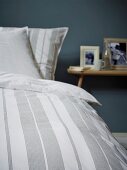 Detail of striped bed linen and bedside table in background
