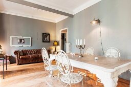 White metal chairs around dining table in front of brown leather couch in room with walls painted light grey