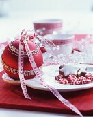 Verzierte rote Weihnachtskugel mit beschriftetem Schleifenband als Tischdekoration