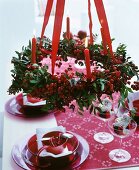 Rot-weiss gedeckter Weihnachtstisch unter aufgehängtem Adventskranz mit Beerenzweigen und brennenden Kerzen