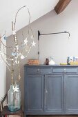 Paper decorations hanging from branch in front of grey cabinet