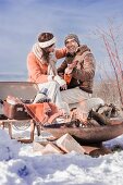 Frau und Mann mit Gitarre beim Winter-Picknick in verschneiter Landschaft