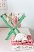 Dolls' clothes on green, wooden, doll's drying rack next to folded blankets and cushions for dolls' house