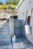 Outdoor shower on white wooden wall next to steps and retaining wall in a hillside garden