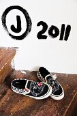 Shoes on rustic wooden step below black letters and digits painted on white wall