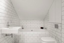 Bathtub and toilet in white-tiled attic bathroom
