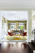 Vorraum mit breitem Durchgang und Blick in Wohnbereich mit Retro Ledersesseln und gelbem Teppich