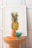 Cork side table with ceramic bowls and vase in front of picture with pineapple motif