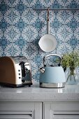 Retro teakettle and toaster on kitchen counter in front of blue and white wallpaper
