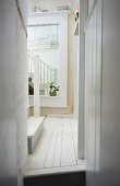 Narrow hallway in rustic house with white wooden floor and large mirror on wall in background