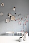 Arrangement of vases and branches of red berries in front of decorative plates and retro lamp on grey wall