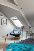 Sessel und Dreibeintisch unter dem Dachfenster im Schlafzimmer