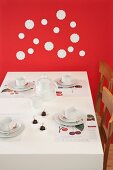 Table set for afternoon coffee with cherries against red wall decorated with white doilies