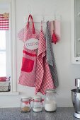 Red and white apron and tea towels hanging from vintage pegs with old-fashioned storage jars in foreground