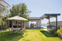 Architektenhaus mit Garten, Sitzplatz unter Sonnenschirm auf Rasenfläche, Außenküche und Meerblick