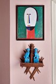 Blue animal figurines on wooden bracket and modern portrait of man on pink wall