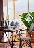 Candlesticks and crockery on side table next to cane chair and houseplant